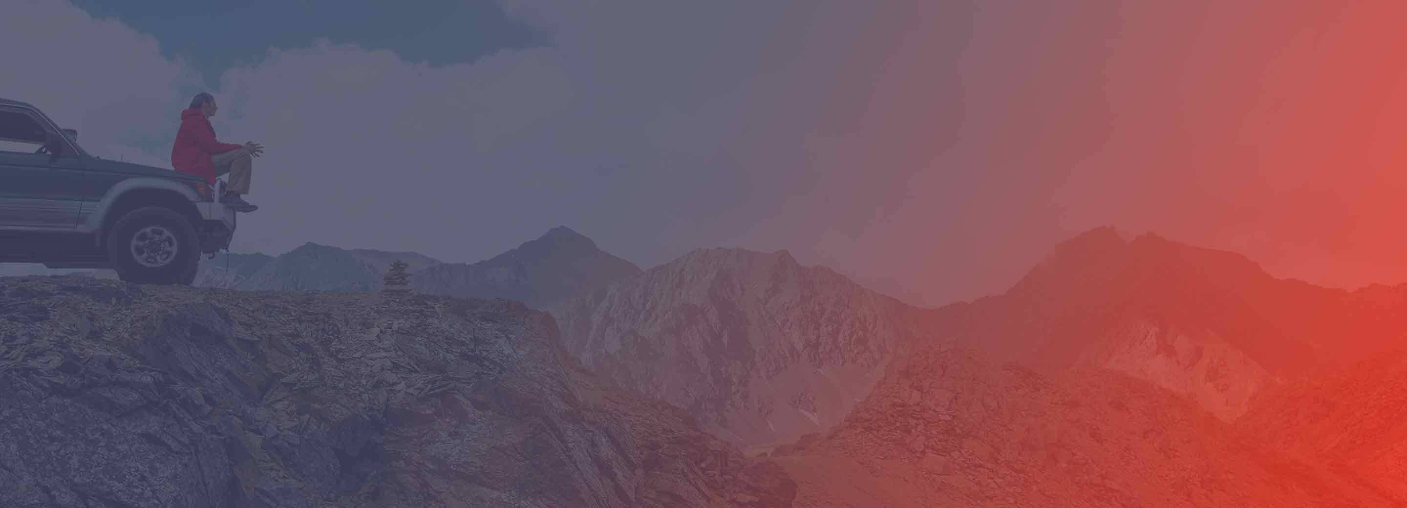 person sitting on car overlooking mountains